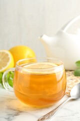 Aromatic tea in cup with lemon and spoon on white marble table, closeup