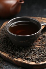 Aromatic black tea in cup and dried leaves on table, closeup