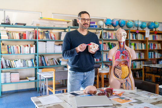 Man teaching biology, pointing at a skull model in a science classroom