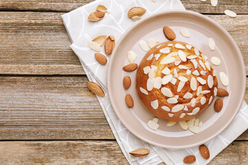 Tasty roll bun with almond flakes and nuts on wooden table, flat lay. Space for text