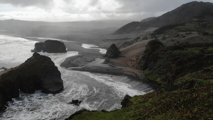 Powerful ocean waves crashing on black sand beach on cloudy day