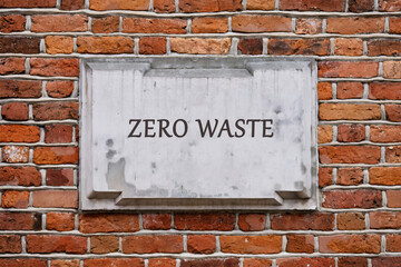 Fototapeta premium The words ZERO WASTE are inscribed on a light grey stone plaque mounted on a red brick wall. A message of environmental responsibility against the backdrop of timeless construction