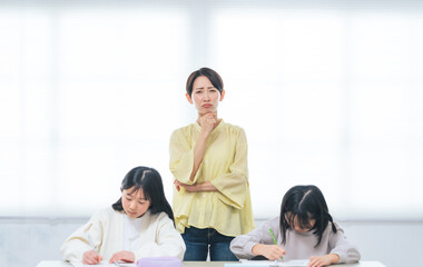 勉強する二人の女の子の後ろで悩む女性