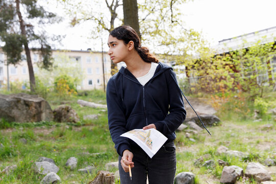 Thoughtful girl holding map and looking away during treasure hunt adventure