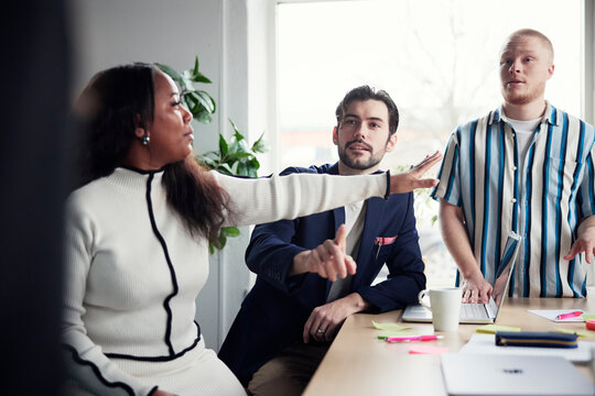 Female manager interrupting male colleagues discussing in debate at office