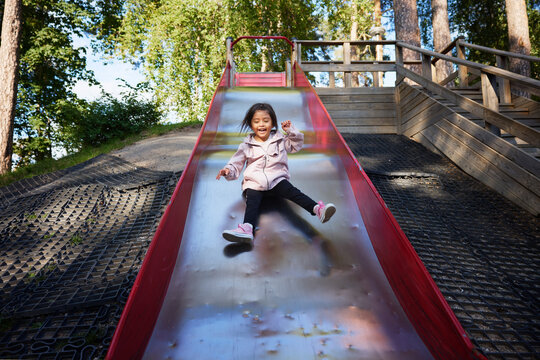 Cheerful girl spending leisure time playing on slide at park