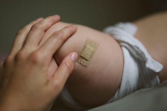 Hand of unrecognizable person touching vaccinated limb of newborn baby