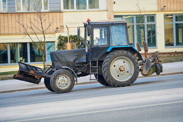 Tractor with snow plow and rotating brush drives along salted city road during winter season, snow...