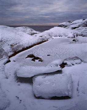 Rock formations covered with snow near sea against sky