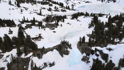 Snowy mountain valley panning showing partially frozen lake and pine trees. Media