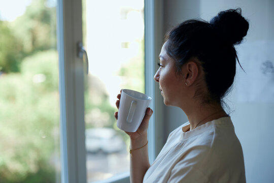 Thoughtful holding mug while looking through window at home