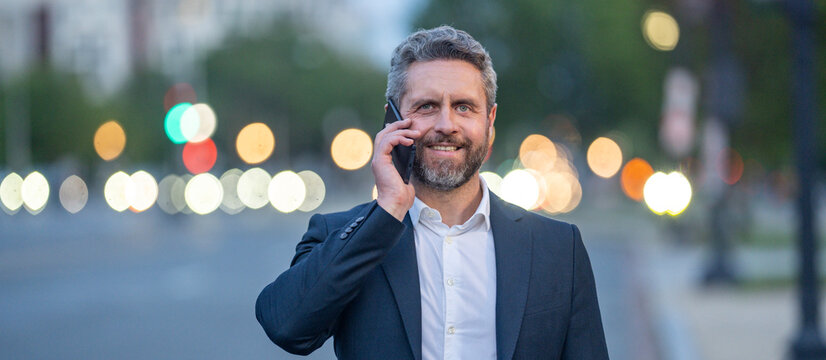 Hispanic business man talking on a smartphone while walking in the city at night. Business late call. Business conversation and overtime work. Business man man in a suit speaking on the phone outdoor.
