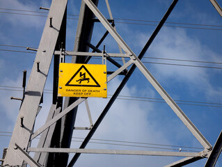 Danger of Death Keep Off warning sign with electrocution symbol mounted on grey electricity pylon...