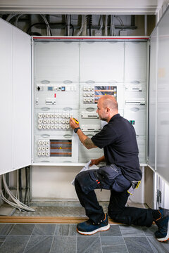 Male electrician examining control panel while kneeling inside factory