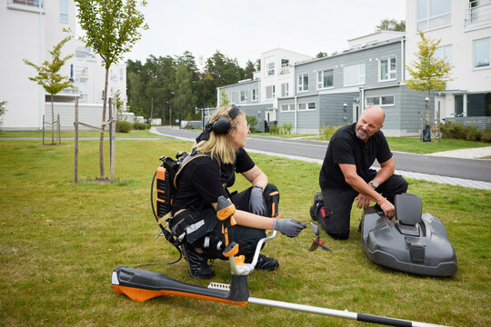 Woman with gardening equipment talking with man while crouching on grass