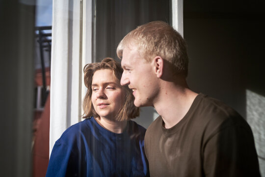 Smiling man spending leisure time with girlfriend near window at home