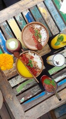 A vibrant and healthy tropical breakfast spread featuring colorful mango and cacao smoothie bowls on a rustic painted wooden table