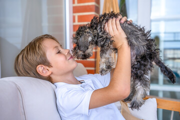 Cute little boy hugging and playing his little puppy dog at home.