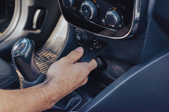 Male hand holds keyless remote by dashboard and start controls in modern car interior, secure entry and ignition concept