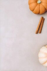 Minimal autumn flatlay with pumpkins and cinnamon sticks placed on a soft beige surface. Clean, warm, seasonal composition perfect for fall and holiday themes.