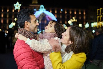 Parents smiling at daughter in festive Christmas square at night