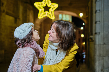 Caucasian mother watching daughter admire Christmas star lights at night