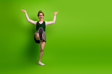 Energetic student in uniform happily posing against vibrant green background, displaying youthful...
