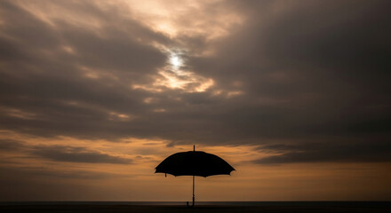 Silhouette of an Umbrella Against a Cloudy Sky at Sunset