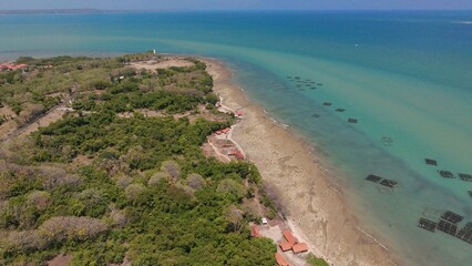 An aerial view of coastline with a beach and what appear to be turquoise water with lush vegetation