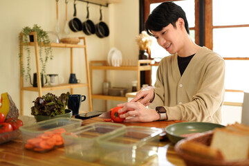 A man is cutting a tomato in a kitchen. He is smiling and seems to be enjoying the process