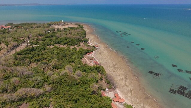 An aerial view of coastline with a beach and what appear to be turquoise water with lush vegetation
