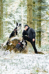 schwarz gekleideter Mann Hundebesitzer mit zwei Hunden Border Colli in tricolor und Merle odd-eyed  im Wald posierend auf einer Erh&ouml;hung