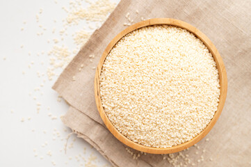 White sesame seeds in wooden bowl on natural linen cloth and white background. Organic sesame, cooking ingredient, Asian seasoning, source of calcium. Space for text