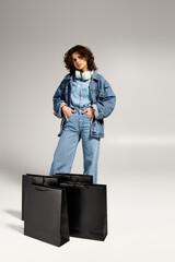 Fashionable young woman showcases her style with shopping bags in a modern studio setting