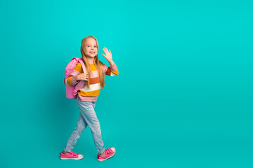 Smiling young girl with pink backpack waving happily in casual outfit on a turquoise background