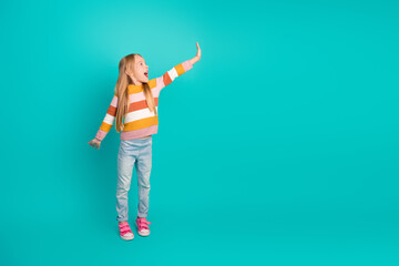 Energetic young girl gesturing on a turquoise background, displaying enthusiasm and happiness, dressed in colorful casual clothes.
