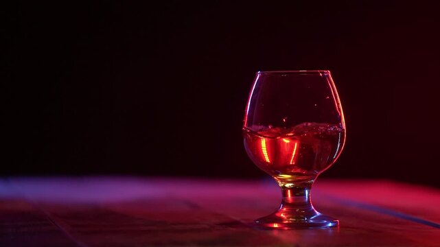 Slow motion shot of ice cubes falling into glass with alcohol on the dark background. Ice cube falling in the glass of brandy with splash. Copy space.