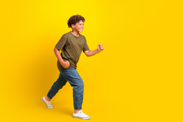 Fototapeta premium Funny energetic boy in casual khaki tee and jeans runs across a bright yellow background for a lively lifestyle and fitness style promo