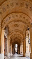 Historic vaulted corridor with patterned ceiling, arches and hanging lanterns in warm stone architecture