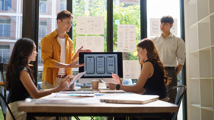 Group of designers discussing and reviewing mobile application prototypes laid out on the table during a creative brainstorming session.