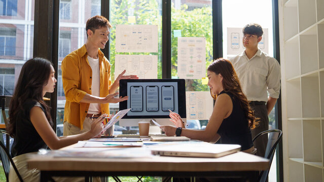 Group of designers discussing and reviewing mobile application prototypes laid out on the table during a creative brainstorming session. - Powered by Adobe