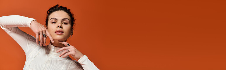 Obraz premium Beautiful young woman showcases bold fashion against a vibrant orange backdrop