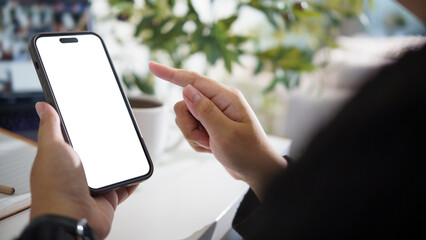 Close up of hands interacting with mobile phone in cozy home office, blank screen for app mockup or web design.