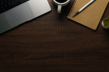 Top view of workspace with laptop, coffee cup, and notebook on dark wooden desk.