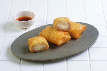 Golden brown crispy fried dimsum or dimsum goreng keju served on a dark grey plate with chili sauce. Perfect Asian snack or appetizer for culinary and food photography content.