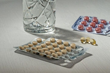 Pills in blisters and a glass of water on the table.
