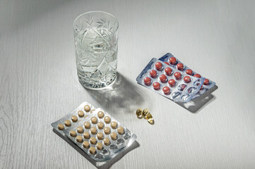 Pills in blisters and a glass of water on the table.