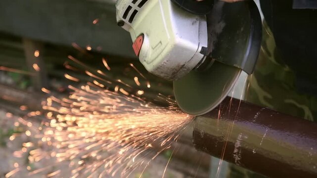 Worker cutting metal pipe with an angle grinder, producing bright sparks during industrial work process. Strength, precision, and craftsmanship. Hard work and labor. For a construction or tool company