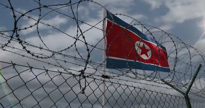 North Korea waving flag on country border concept. Korean blowing banner with barbed wire fence.