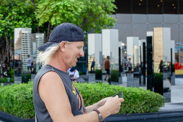 Fototapeta premium A smiling mature man using a phone in front of a mirrored urban park installation
